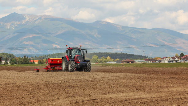 拖拉机在空地上播种，背景是村庄的房子和山。图片下载