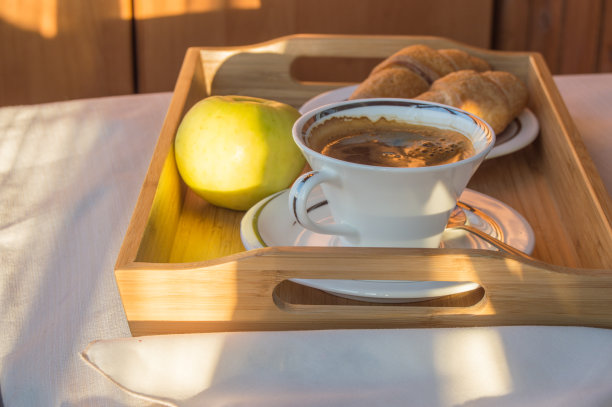 阳光下的阳台上，美味的早餐，咖啡，牛角面包，木托盘上的苹果图片下载