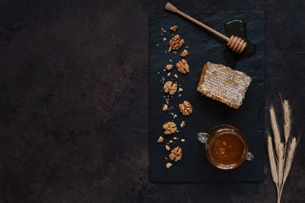玻璃锅，在石板上放新鲜的天然蜂蜜，蜜糖和核桃。俯视图，特写，平躺在黑暗的背景上图片下载