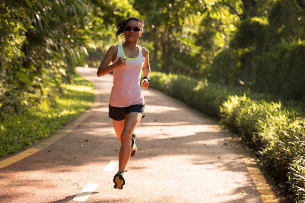在夏季公园小径上跑步的女性。健康的健身女人在户外慢跑。图片下载