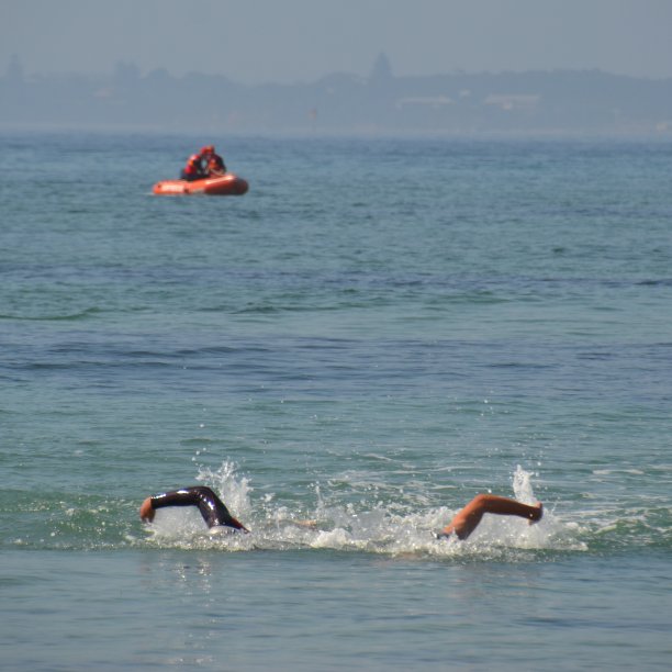 两名游泳运动员以救生船为背景，在开放水域的海洋中进行游泳比赛，比赛到海滩图片下载
