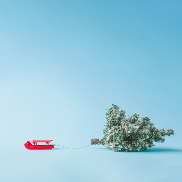 红色圣诞老人的雪橇拉着圣诞树与明亮的蓝色背景。图片下载