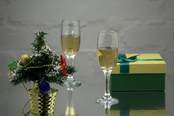 白色的木桌上放着几只放着金色香槟的玻璃杯，红色的背景上放着一根云杉枝做的圣诞球。新年快乐概念照片。浅景深。图片下载