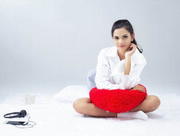 美女坐在床上，把红色的枕头放在她的腿上，开心的感觉，放松的时间图片下载