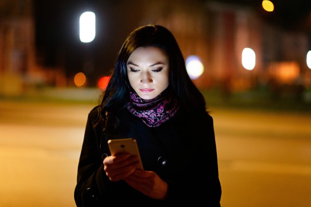 年轻的黑发女子在晚上使用手机。图片下载
