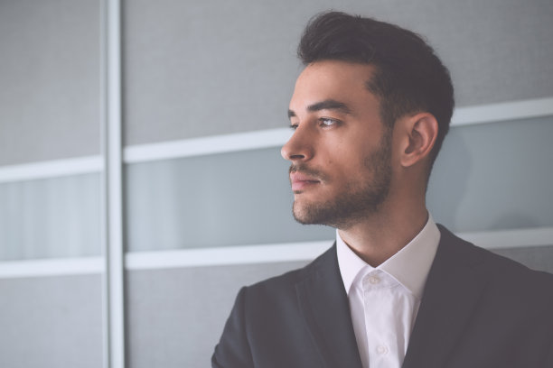 美丽的肖像，严肃思考的商人西装看着一边在办公室的背景。图片下载