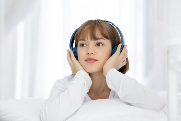 美丽迷人的亚洲年轻女子听音乐和躺在床上在卧室的感觉，所以放松和舒适，选择性的焦点图片下载
