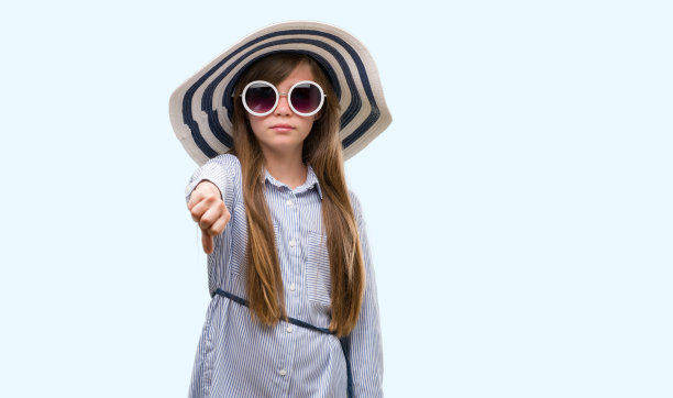 年轻的金发小孩戴着帽子和太阳镜，愤怒的脸，消极的迹象显示不喜欢拇指向下，拒绝概念图片下载