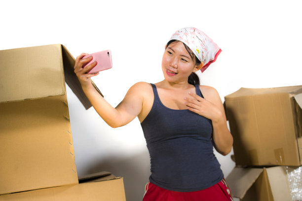 年轻美丽和快乐的亚洲韩国女人兴奋地在家里客厅地板从纸箱搬到新公寓的行李与手机自拍照片图片下载