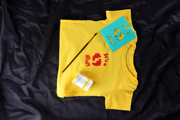 用手工画缝制儿童t恤。深色背景上的黄色织物。裁剪的过程。t恤与图片。黑色背景上的黄色t恤图片下载