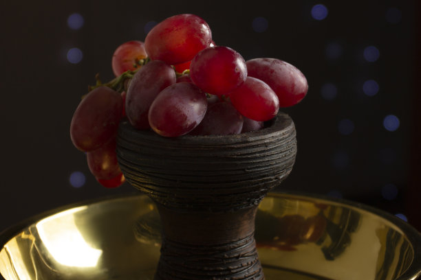 健康的生活方式。红色的葡萄在碗水烟代替烟草在黑暗的背景与灯光图片下载