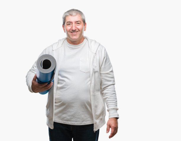 英俊的老男人拿着瑜伽垫在孤立的背景与一个快乐的脸站着，微笑着自信的微笑显示牙齿图片下载