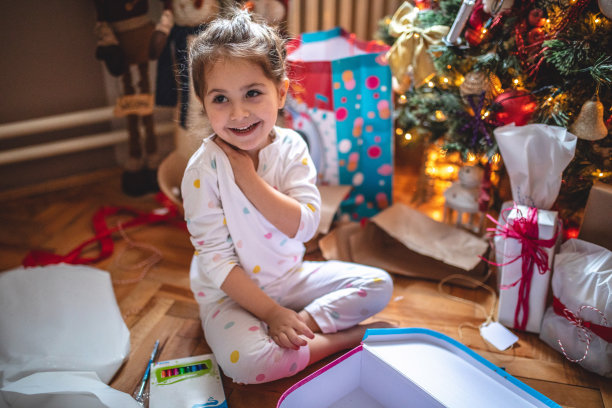 穿着睡衣的美丽微笑的孩子在树下打开礼物图片下载