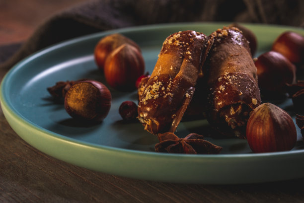 横向照片的几个甜卷塞满了奶油和巧克力在末端。蓝色的盘子里有糖果和几颗生榛子。盘子是在木板与复古的颜色。图片下载