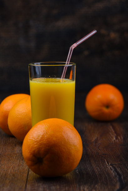 有选择性的重点。玻璃杯里的橙汁和木制背景上的整个橙子图片下载