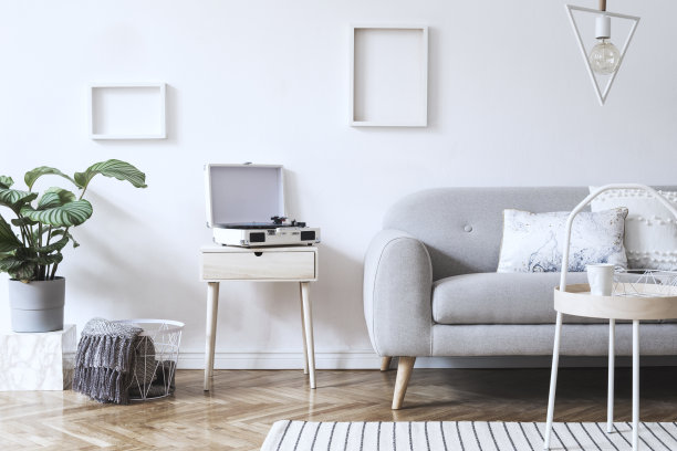 时尚的斯堪的纳维亚白色室内设计沙发，热带植物，枕头，毯子，留声机和模拟相框。白色的背景墙，棕色的拼花地板和现代的三角灯。图片下载