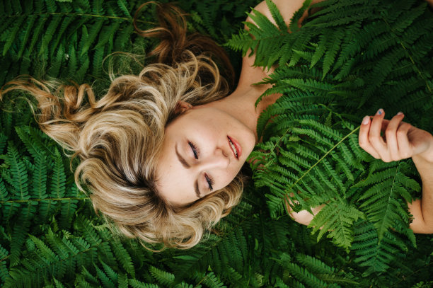 一个美丽的女孩躺在蕨类植物里。图片下载