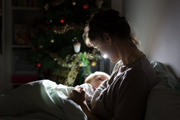 年轻美丽的母亲，在昏暗的灯光下给她的新生儿喂奶。妈妈母乳喂养孩子图片下载