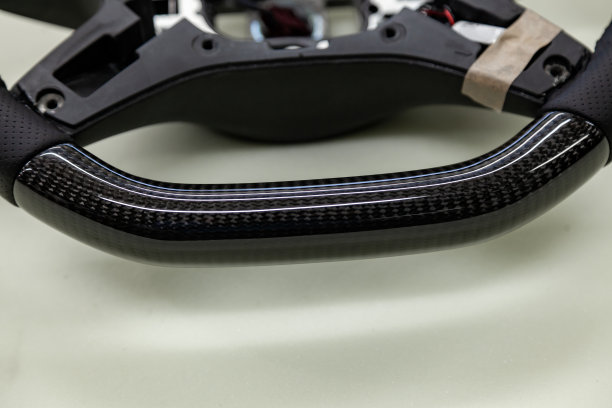 汽车内部的细节元素是一个不同寻常的碳方向盘缝合紫色线从真正的黑色皮革在一个汽车修理车间的特写。图片下载