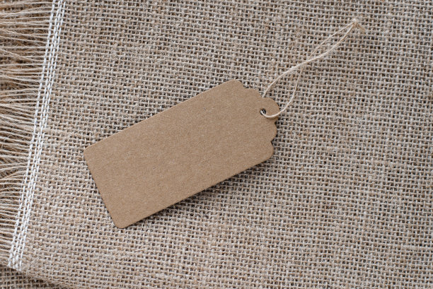 粗布的背景上有绳子的空纸标签。回收纸板标签。折扣价格标签，礼品标签，销售标签，农产品标签。图片下载