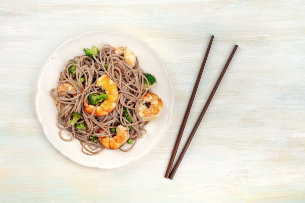 这是一张荞麦面、虾和蔬菜的头顶照片，用筷子在苍白的木制背景上从上方拍摄图片下载