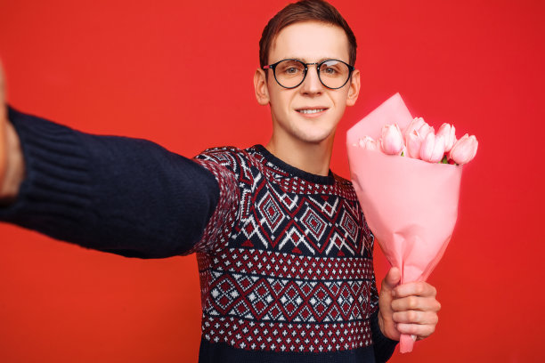 一名戴眼镜、手捧鲜花的男子用智能手机拍下了自己的照片，背景是红色图片下载