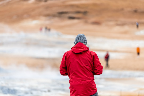一名身穿红色夹克的男子背对着Myvatn湖地热景点附近的间歇泉看风景图片下载