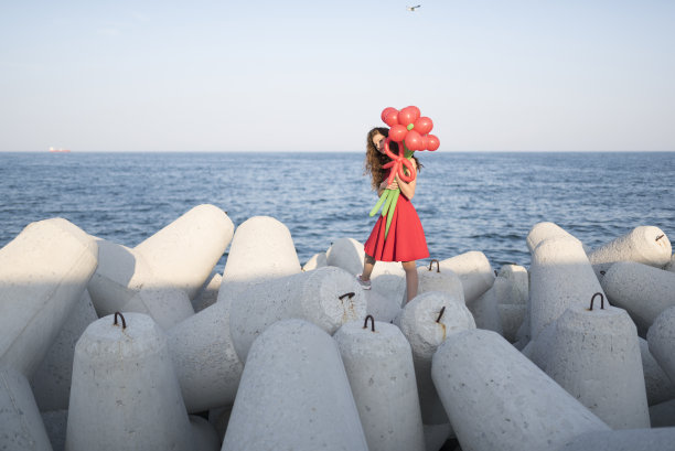 穿着红衣服的害羞女士在海边捧着一个大气球图片下载