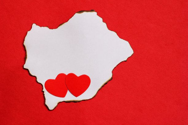 两颗红心躺在一张烧过的白纸上。爱的概念。图片下载