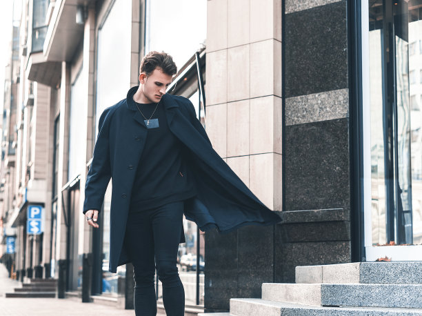 年轻的时尚男子穿着黑色外套和黑色牛仔裤，走在街上。都市背景下留着现代发型的大胡子年轻人。图片下载