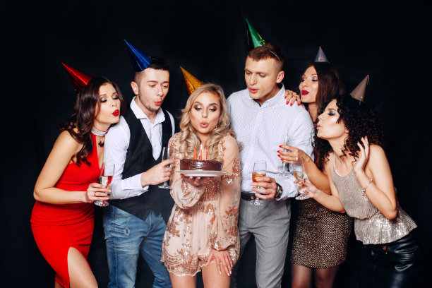 朋友的生日聚会。肖像迷人的女孩吹蜡烛在生日蛋糕周围的朋友在聚会图片下载