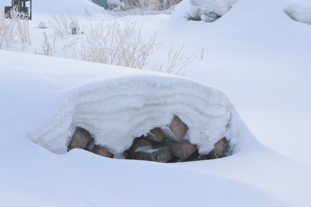 建筑用的原木埋在雪下。横向框架。过冬时木料没有搬走。他们躺在厚厚的积雪下的地上。图片下载