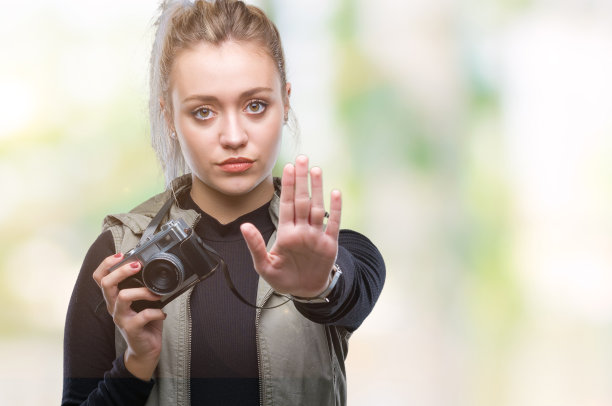 年轻的金发女子用老式相机在孤立的背景下拍照，张开手做着严肃和自信的表情，防御手势图片下载