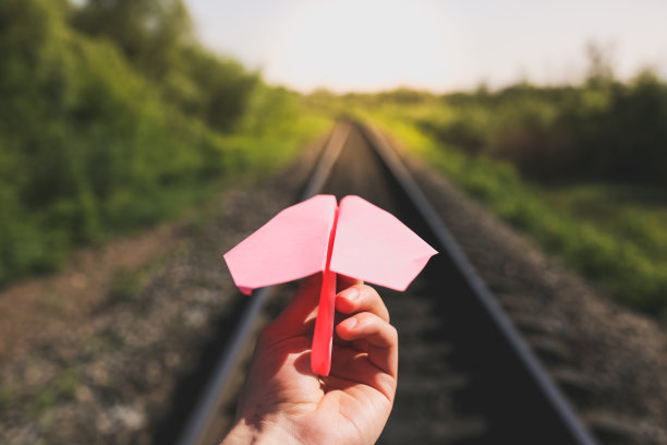 那家伙拿着一架粉红色的手工飞机。自由概念照片与轨道在绿色领域。铁路运输行业。夏日空旷的道路。旅行的生活动力。图片下载