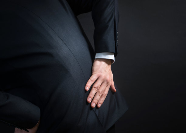 穿着西装后背疼的商人。双手握住下背部，痛苦地弯腰图片下载