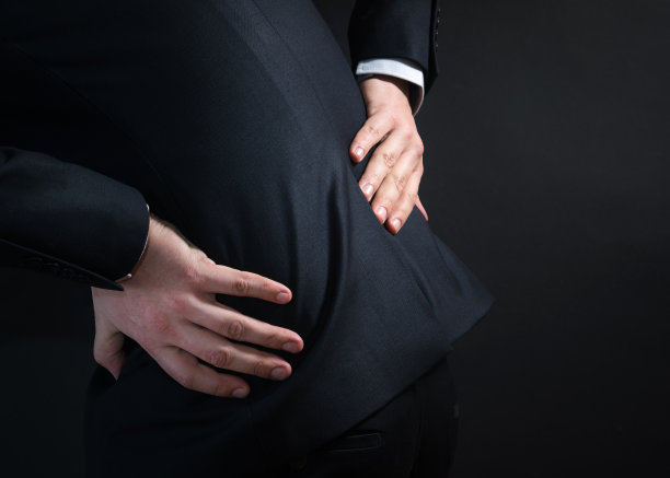 穿着西装后背疼的商人。双手握住下背部，痛苦地弯腰图片下载