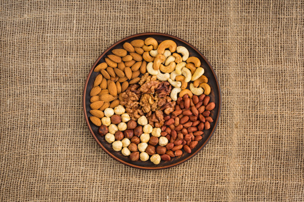 各种各样的健康坚果放在一个盘子上，背景是粗麻布图片下载
