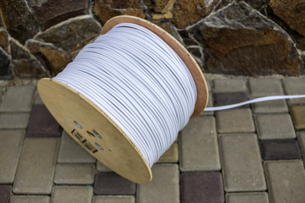 大卷白色工业电缆在大型木制卷轴户外阳光人行道石栅栏背景。专业施工现场电缆，接线可靠耐用。图片下载