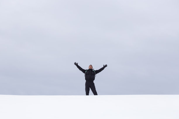 成年男子徒步旅行者张开双臂，望着白雪覆盖的空旷田野图片下载