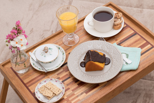 的生活方式。早餐在床上，有橙汁，茶，漂亮的老式黄油盘，美味的蛋糕，巧克力糖霜和精致的花在托盘上图片下载