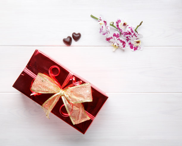 白色木桌，红色礼盒，金色蝴蝶结和兰花花。前视图。平的。副本的空间。图片下载