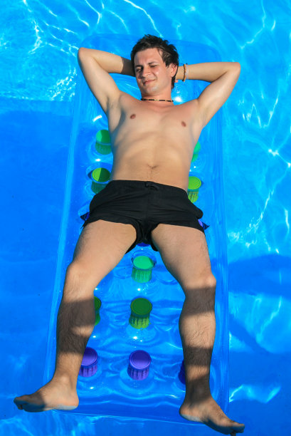 环游希腊。一个年轻人在一个蓝色的水池里的水床垫上游泳图片下载