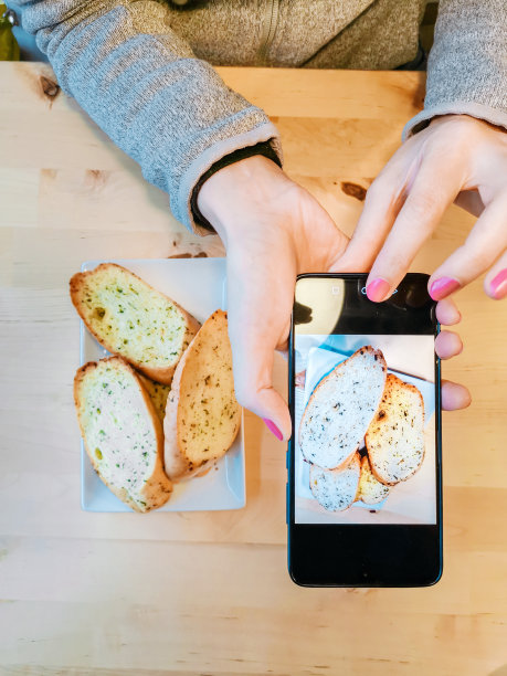 一个女人拿着手机拍大蒜面包图片下载