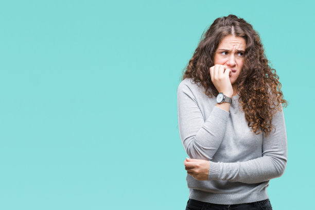美丽的黑发卷曲的年轻女孩穿着毛衣在孤立的背景看起来紧张和紧张的手在嘴咬指甲。焦虑的问题。图片下载