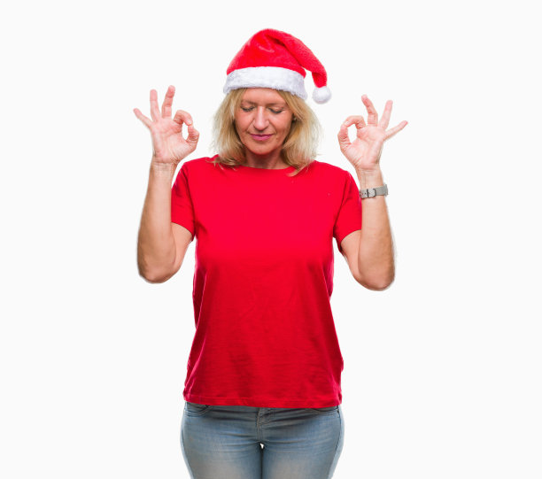 中年金发女人戴着圣诞帽在孤立的背景放松，微笑着闭上眼睛做冥想手势与手指。瑜伽的概念。图片下载