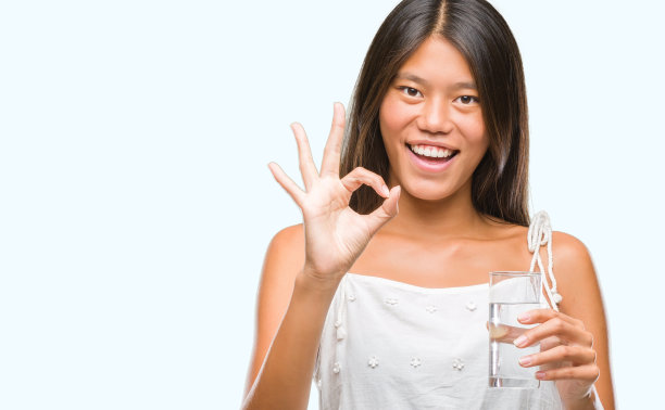年轻的亚洲女子在孤立的背景下喝着一杯水，用手指做着ok的手势，很好的象征图片下载