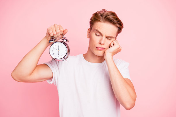 漂亮可爱的可爱的有吸引力的英俊的严肃的时尚整洁的家伙在白色t恤手拿着看时钟孤立在粉色柔和的背景图片下载