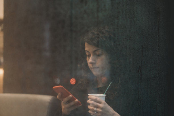 一个下雨天，一个沉思的女人在商店橱窗边用智能手机发短信图片下载