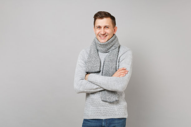 微笑的年轻人在灰色毛衣，围巾手拉手交叉孤立在灰色墙壁背景在工作室。健康时尚的生活方式，人们真诚的情感，寒冷的季节理念。模拟拷贝空间。图片下载