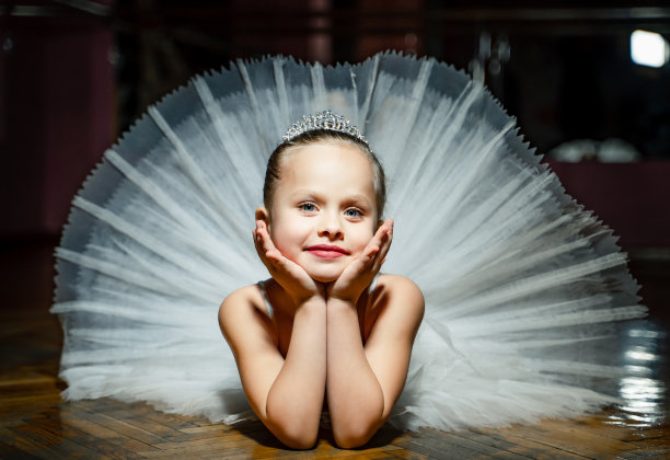 可爱的微笑芭蕾舞的孩子，穿着白色华丽的芭蕾舞裙躺在木地板上，对着镜头摆姿势。图片下载